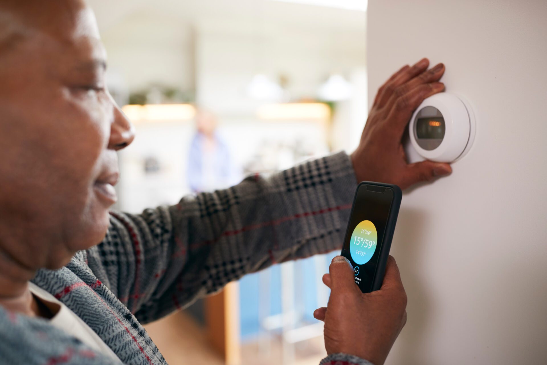 Mature Man Using App On Phone To Control Digital Central Heating Thermostat At Home Mature Man Using App On Phone To Control Digital Central Heating Thermostat At Home